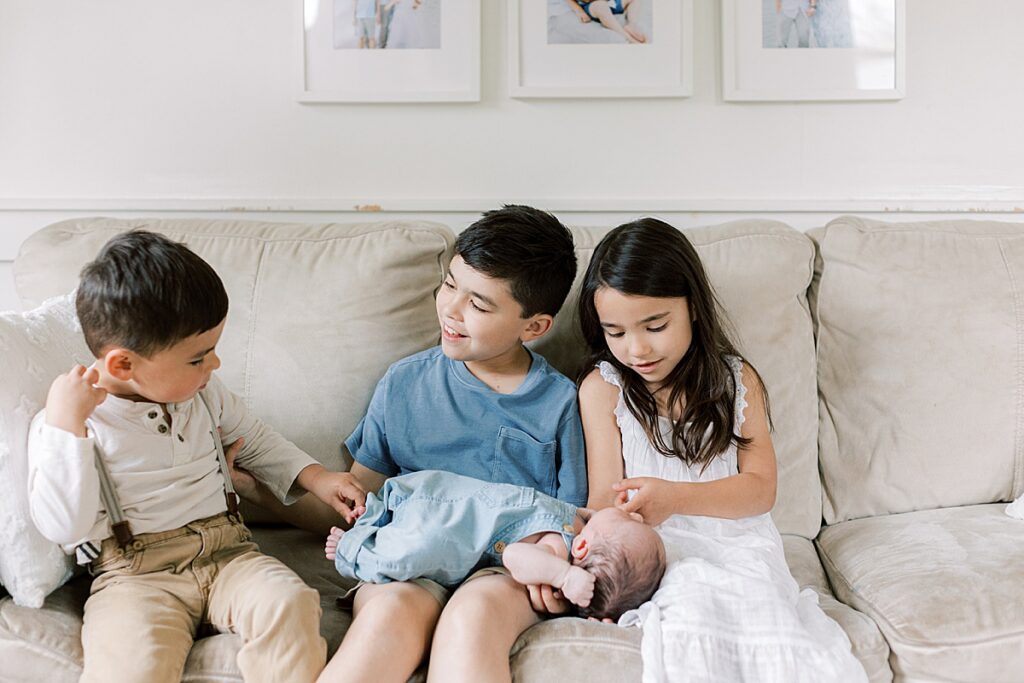 Siblings hold newborn baby on their couch.