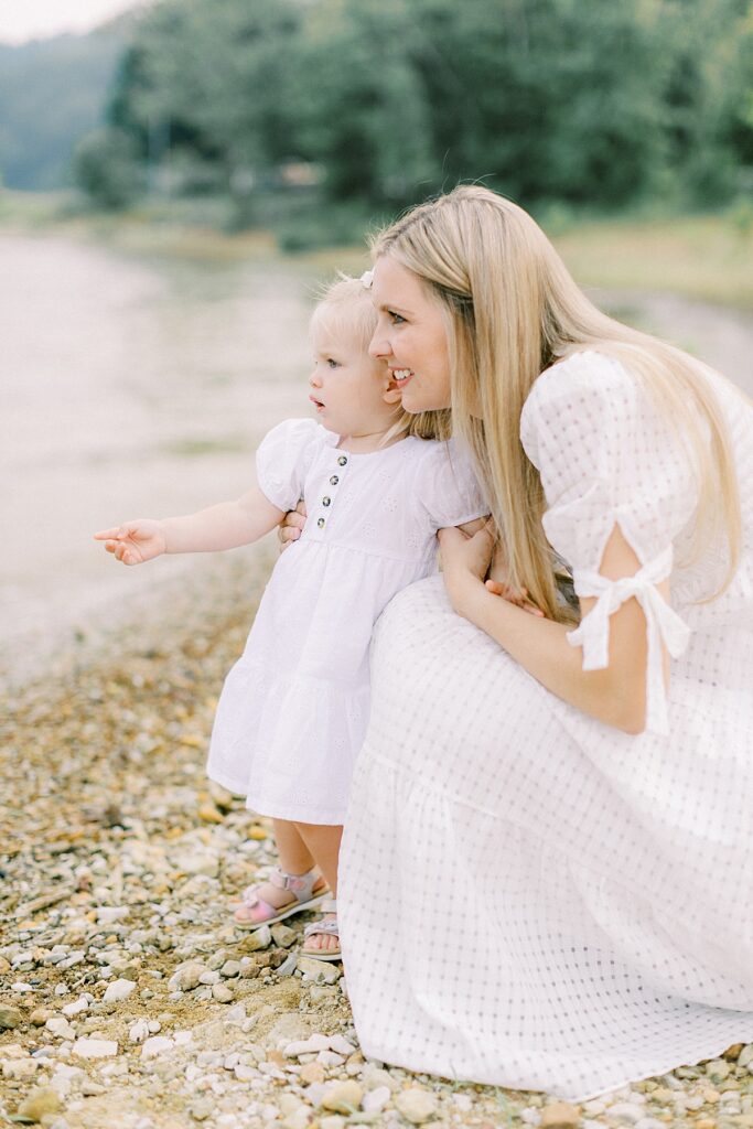 A mother and daughter wearing white look out over a lake in a photo by Katelyn Ng Photography.