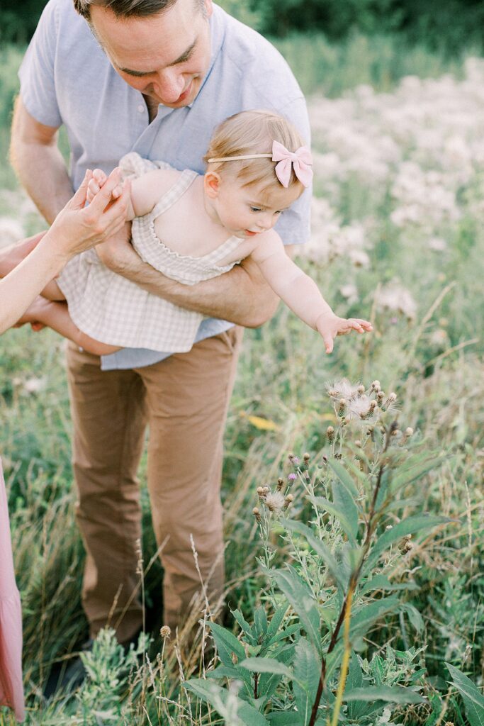 A father helps his daughter reach for a flower in an Indianapolis family photo by Katelyn Ng Photography.