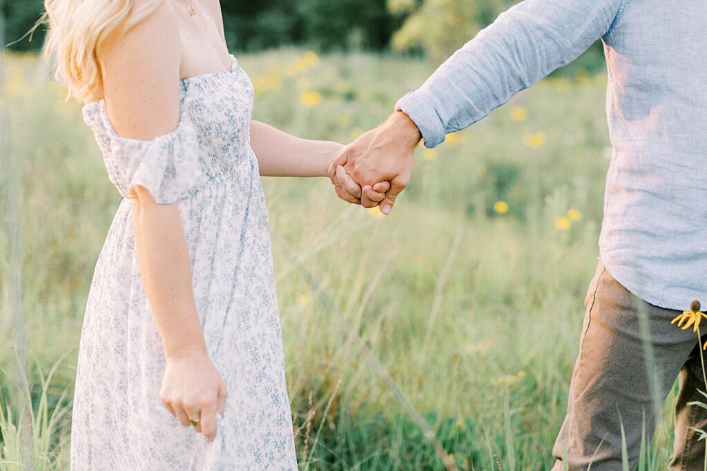 A man and woman walk through a wildflower field together holding hands.