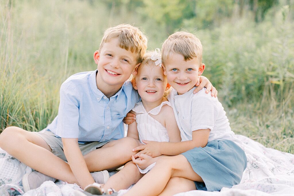 Three children sit a field posing for a photo by Carmel, Indiana family photographer Katelyn Ng Photography.