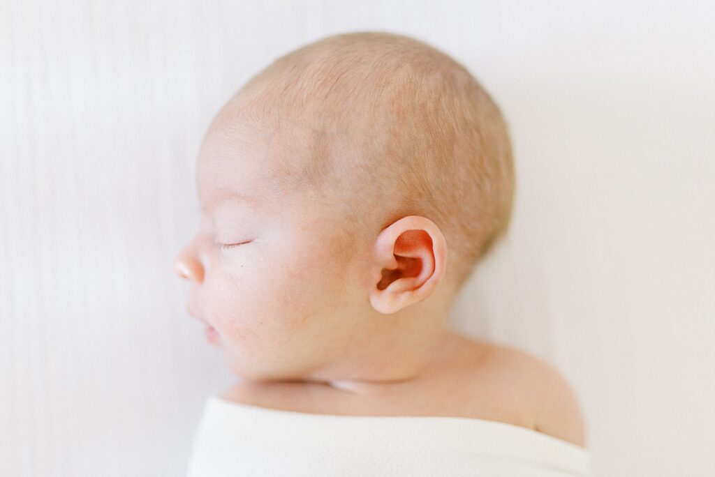 Newborn baby girl lies on a white blanket in a newborn photo by Katelyn Ng Photography