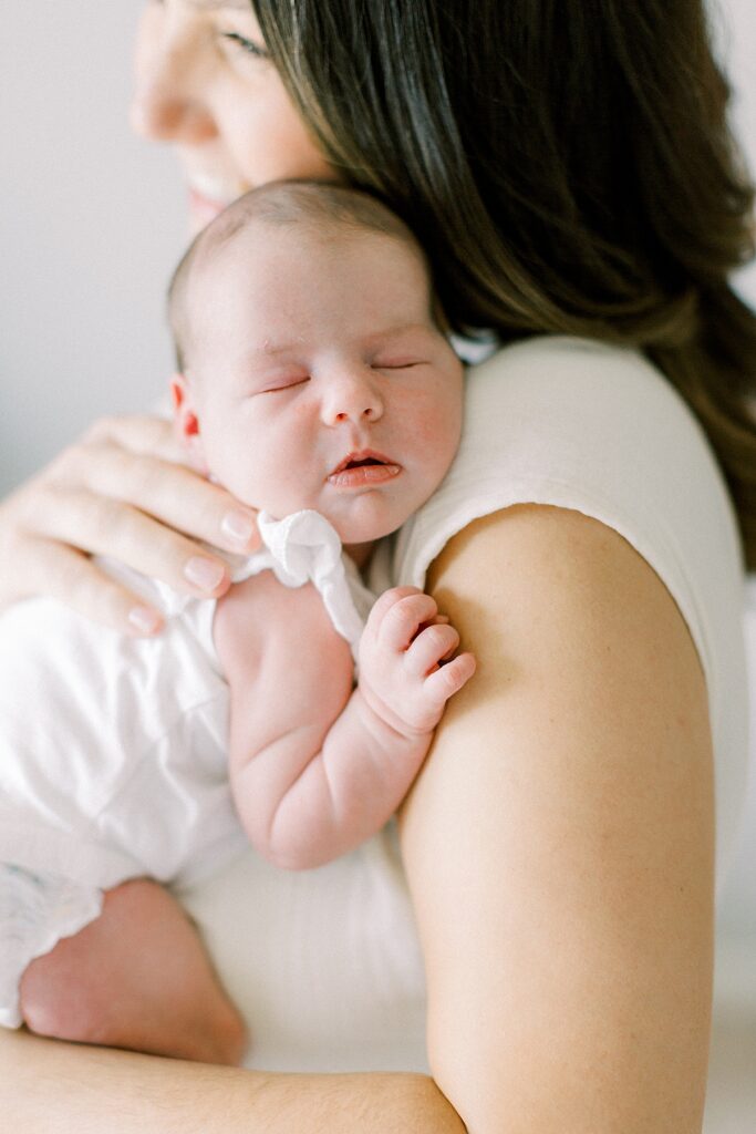A woman wearing a white dress holds her newborn daughter on her shoulder.