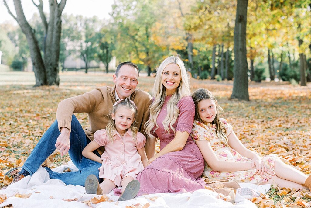 A family sits, posed on a white blanket in a fall family photo in Carmel Indiana.