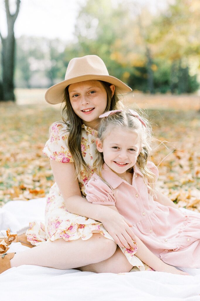 Two little girls dressed in florals and pink sit in fall leaves in a portrait by Katelyn Ng Photography.