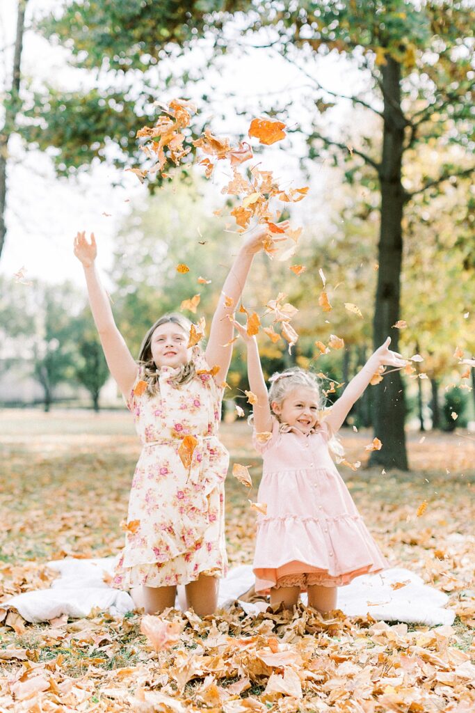 Two girls throw leaves into the air during family pictures in a photo by Katelyn Ng Photography.