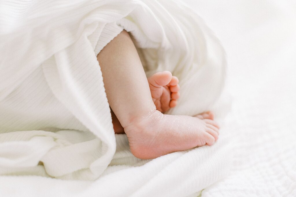 A newborn boy is swaddled in a white ribbed blanket with his tiny toes peeking out on the white blanket.