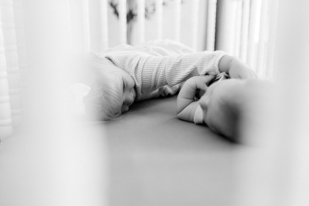 A black and white photo of a little girl lays next to her newborn baby brother. 