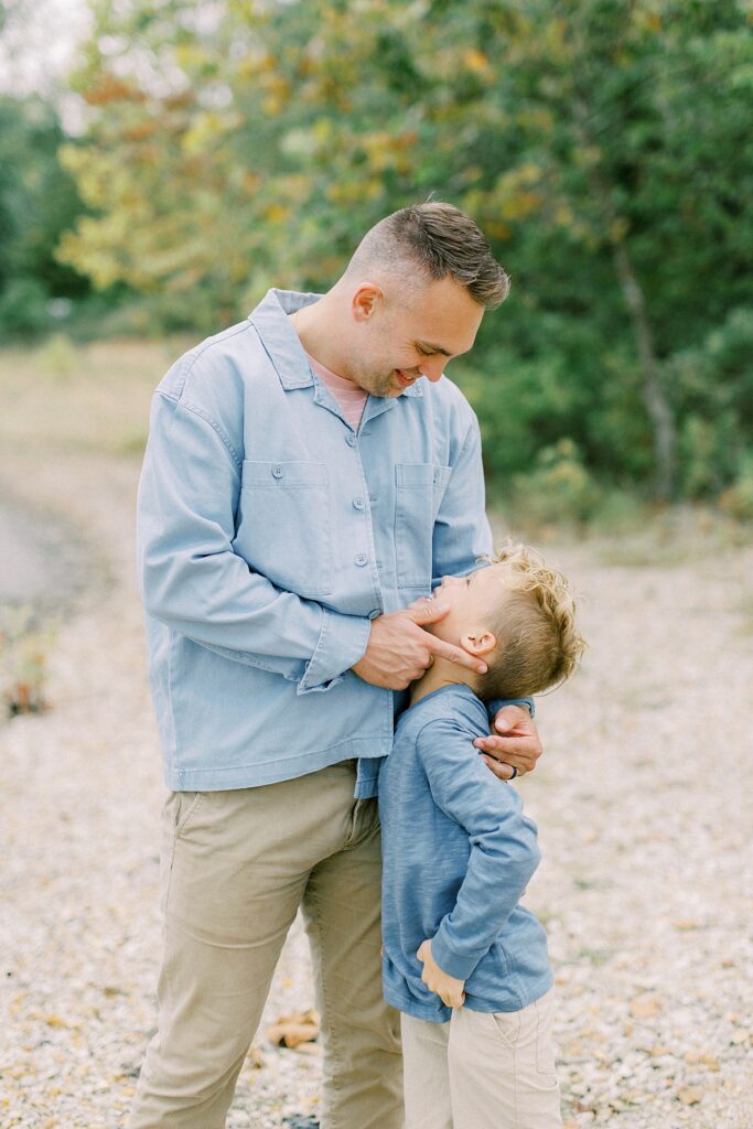 A father looks down holds the face of his young blonde son tenderly in a portrait by Bloomington, Indiana photographer Katelyn Ng.