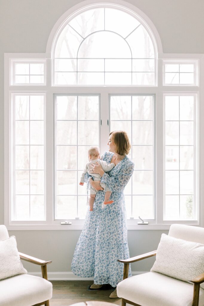 An Indianapolis mother poses for a photo with her baby in front of a large window during their in-home portrait session with family photographer Katelyn Ng Photography.