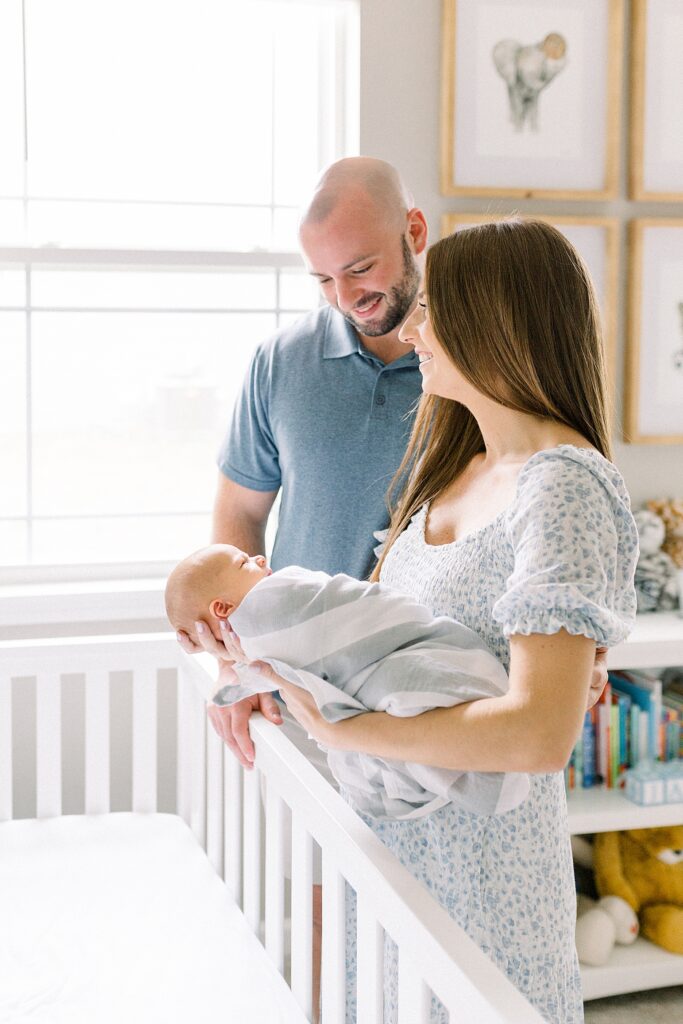 A mother and father stand next to a crib with their newborn baby boy during their in-home newborn photos by Indianapolis photographer, Katelyn Ng Photography.