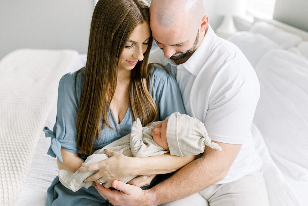 A mother wearing a blue dress and a father wearing a white polo shirt hold their newborn during their in-home newborn photos by Indianapolis based Katelyn Ng Photography.