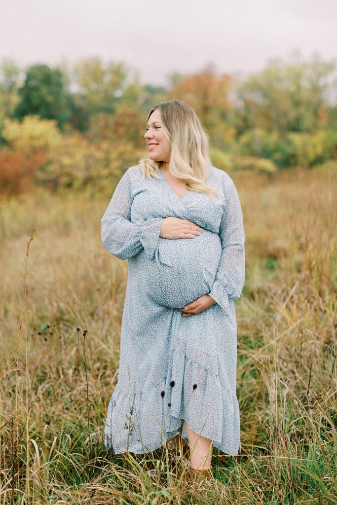 A woman wearing a blue dress walks in a field in Carmel, Indiana during her maternity session with photographer Katelyn Ng Photography.