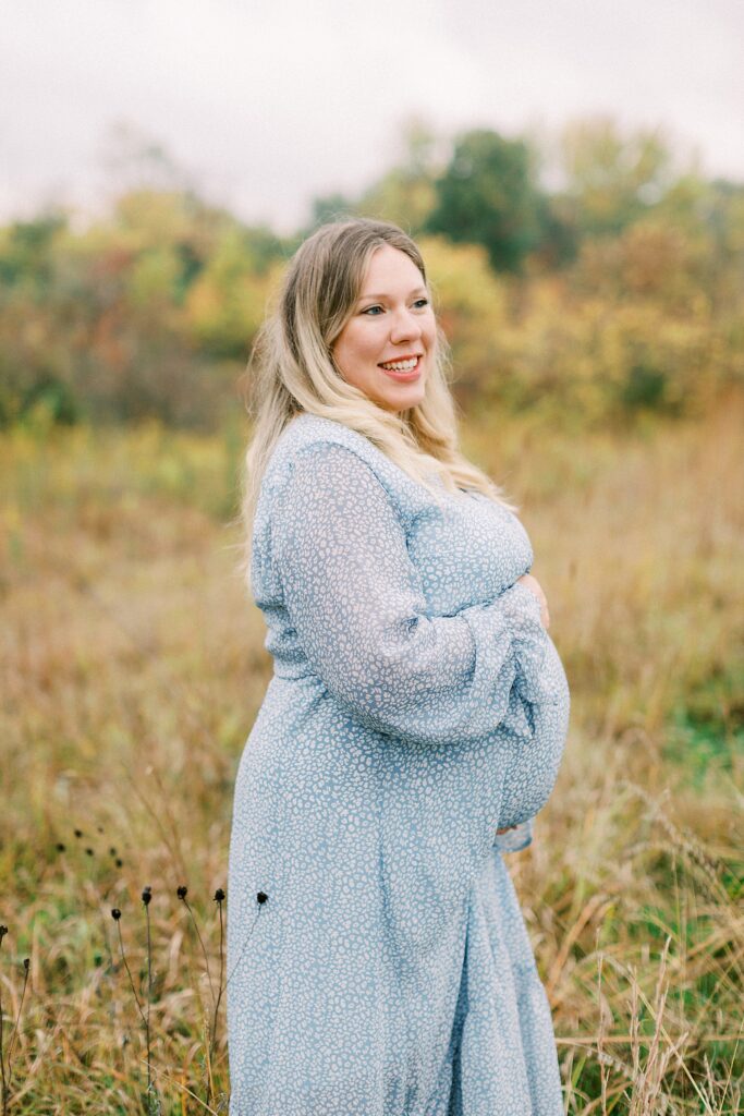 A woman poses in a blue and white dress poses for a maternity photo in Carmel, Indiana.