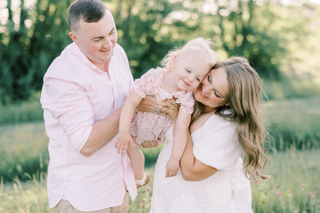 A father and mother hold their daughter between them in an Indianapolis field during their family photos by Katelyn Ng Photography.