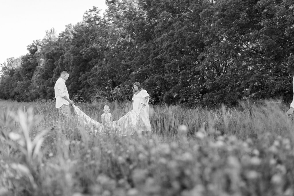 A black and white photo of a family playing with a quilt in a field together in Indianapolis. 