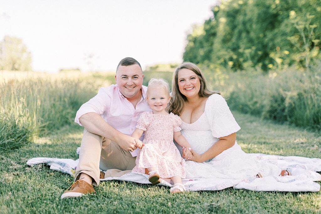 A family of three poses together while they sit on a white blanket in an Indianapolis field. 