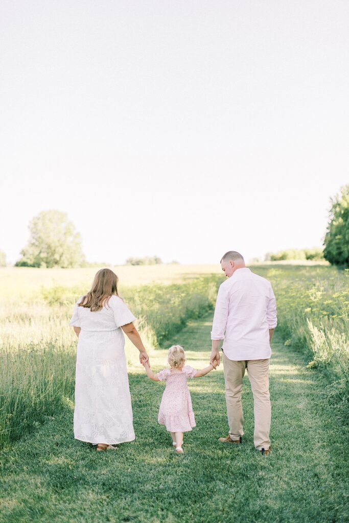 A family of three walk together away from the camera during their family photos.