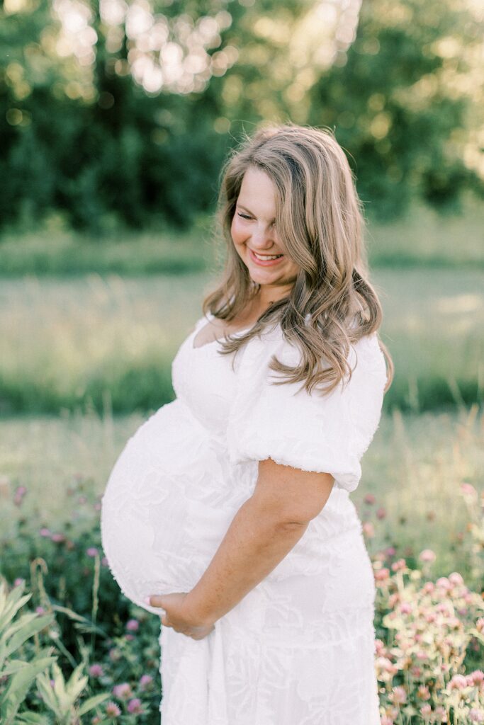 A woman smiles and looks down as she holds her pregnant belly during her maternity photos with Indianapolis family photographer Katelyn Ng.