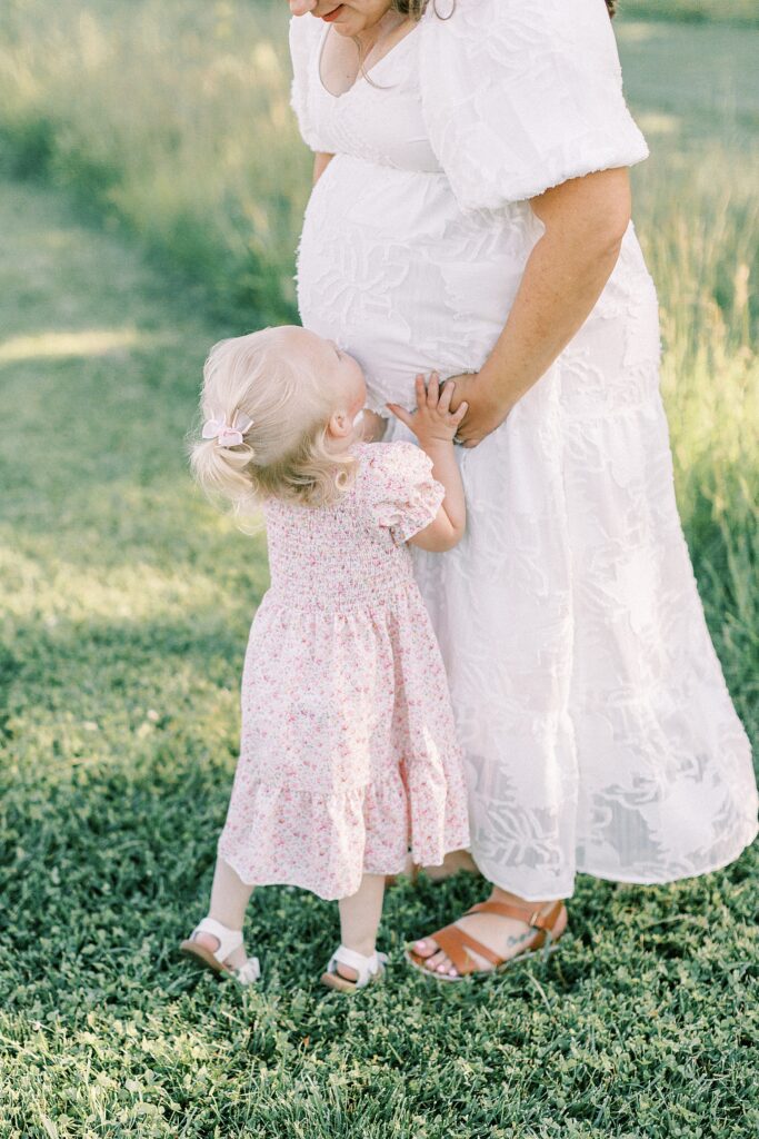 A little girl kisses her mother's pregnant belly in a photo by Katelyn Ng Photography.