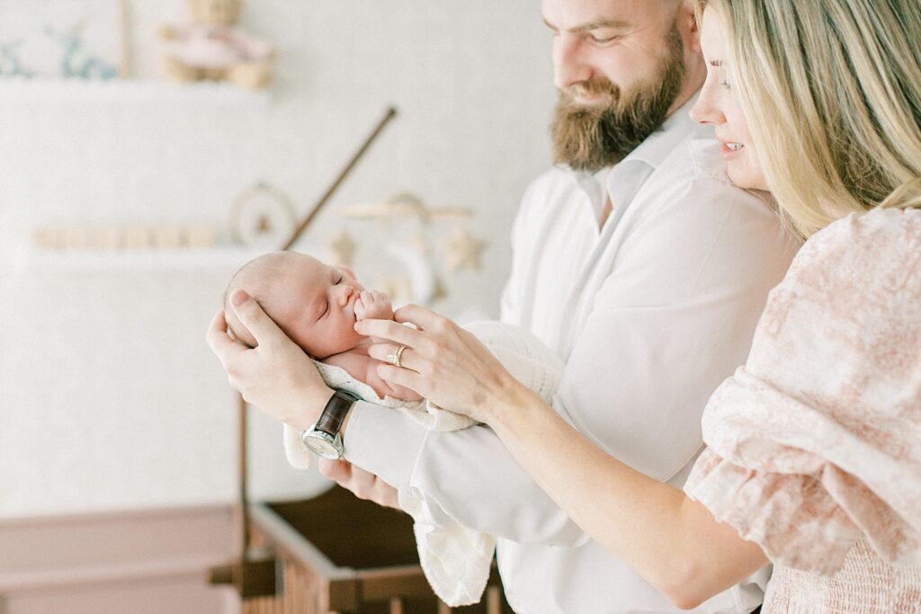 A newborn baby girl holds her hand to her fist as she is craddled in her father's arms during her newborn portrait session in indianapolis.