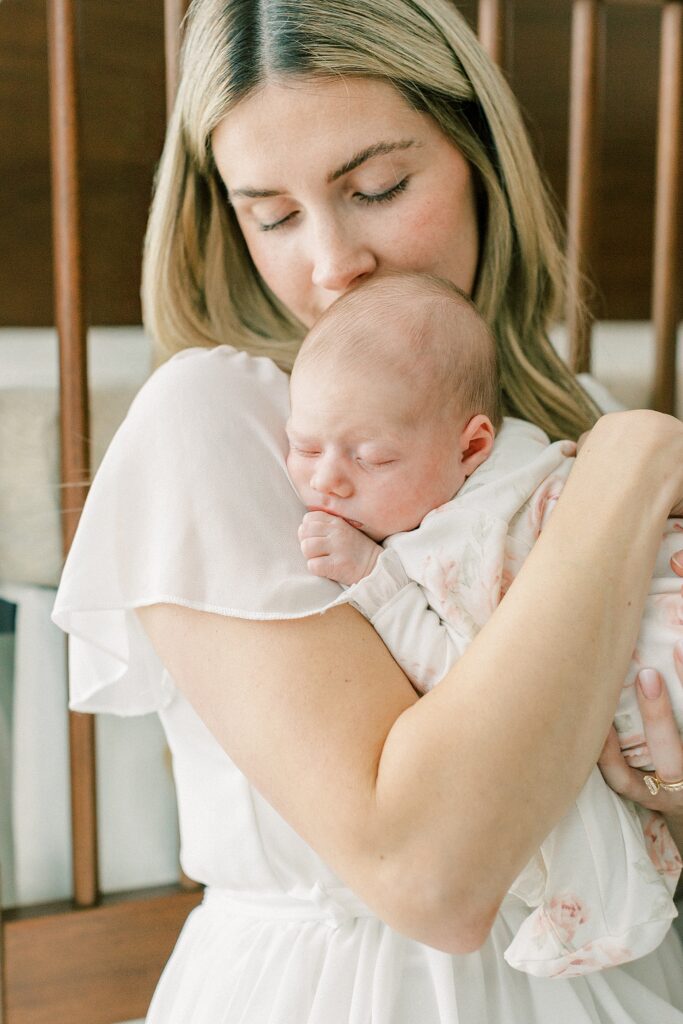 A mother dressed in white kisses the back of her newborn daughter's head in a photo by Indianapolis newborn photographer Katelyn Ng 