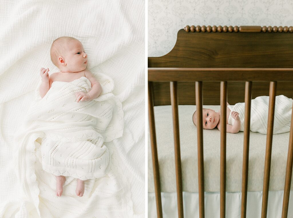 An alert baby girl swaddled in a soft cream blanket peeks out between the crib bars in her nursery.